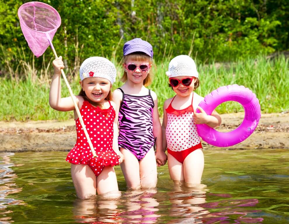 Image of 3 little girls in bathing suits, hats & sun glasses, standing in water.