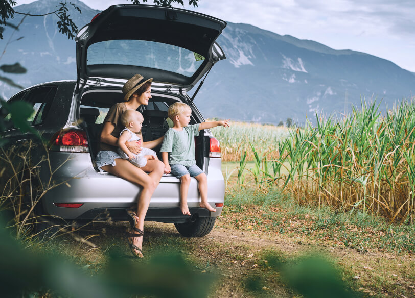 Image of mom and 2 kids sitting in the back of a car with the hatch open.