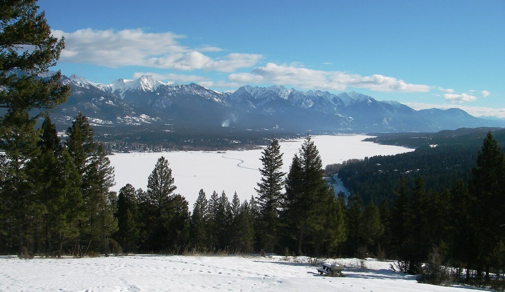 Winter image of frozen lake with snow on it, and snowcapped mountains in the background.