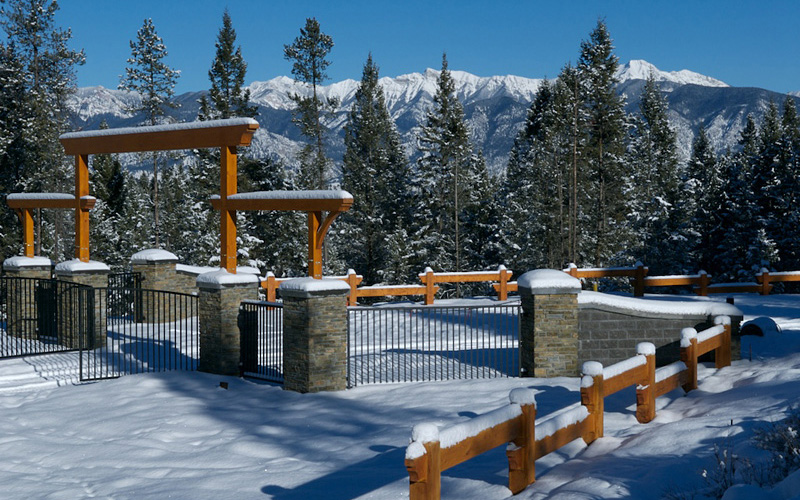 Image of property entrance, stone pillars, wood fence panels, and metal panels with open gate.